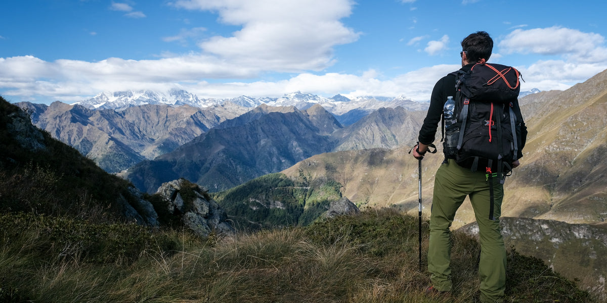 Hiker with trekking poles on a grassy ridge above mountains