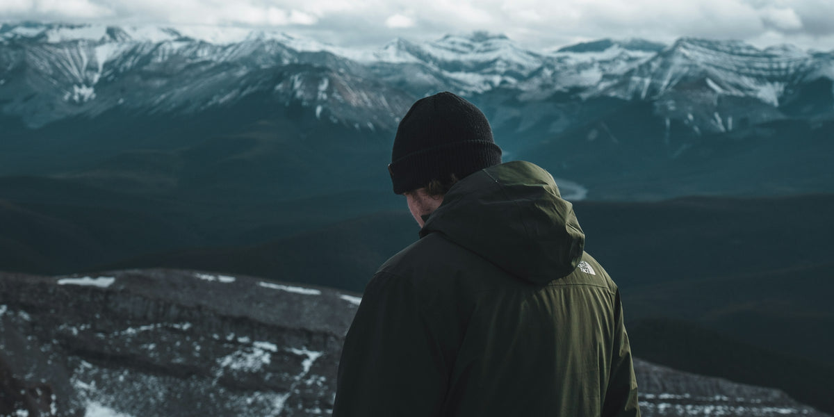 Hiker in a hooded jacket looking out over a mountain range
