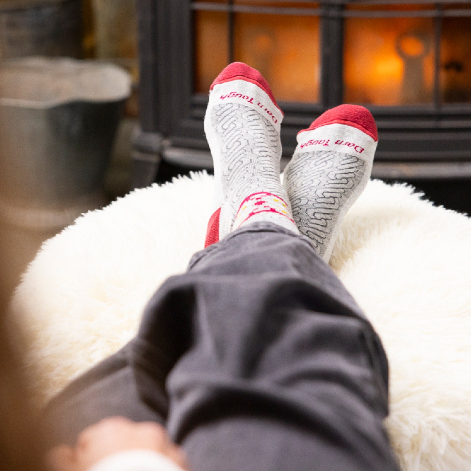 Close up of model's feet in front of a fireplace wearing the Darn Tough Nordic Twist Crew sock in Ash