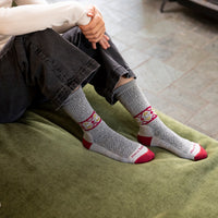Close up of model's feet posed on a couch cushion wearing the Darn Tough Nordic Twist Crew sock in Ash
