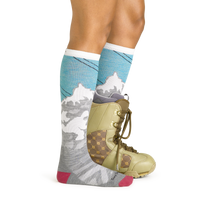 Side studio shot of model wearing the Darn Tough Yeti over-the-calf sock in Aqua with a green snowboard boot on the left foot